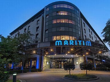 Außenansicht des Maritim Hotel Bremen bei Dämmerung, beleuchtetes Logo und moderne Architektur.