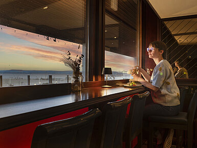 Gast sitzt mit Getränk am Fenster und blickt auf den Sonnenuntergang im Maritim Hotel Travemünde