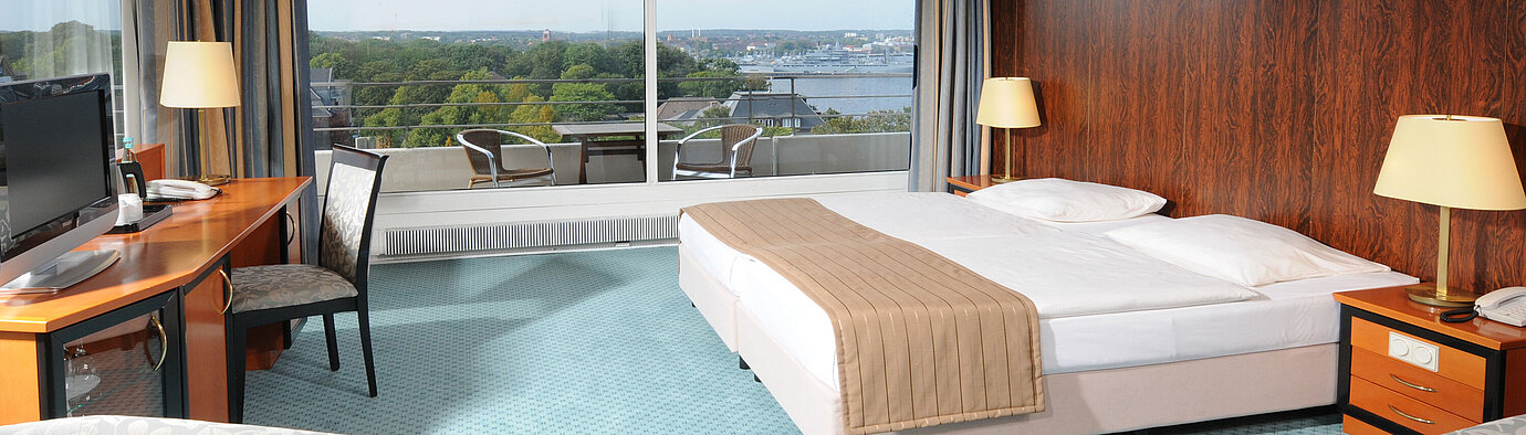 Comfort Doppelzimmer Großzügiges Hotelzimmer mit Doppelbett, Sitzbereich und weitem Ausblick auf Kiel durch die große Fensterfront.