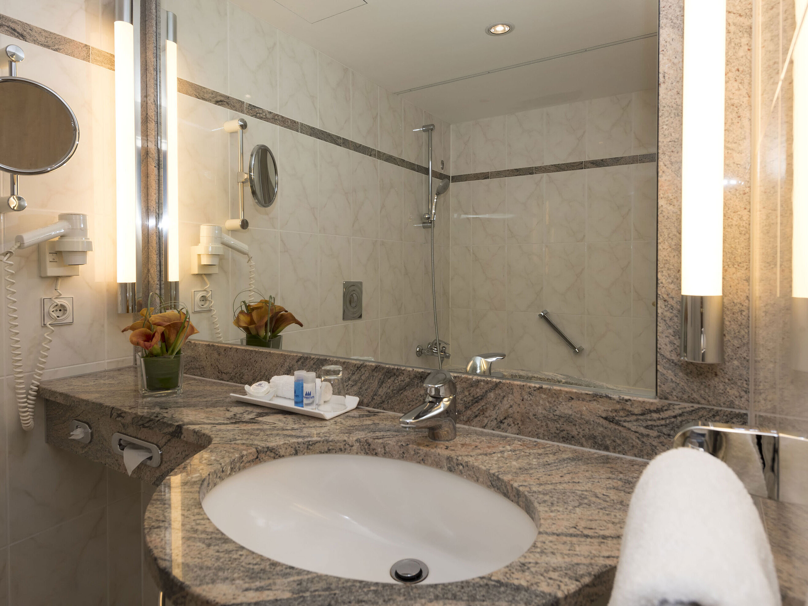 Modernes Badezimmer im Maritim Seehotel Timmendorfer Strand mit Granitwaschtisch, Spiegel und Dusche.