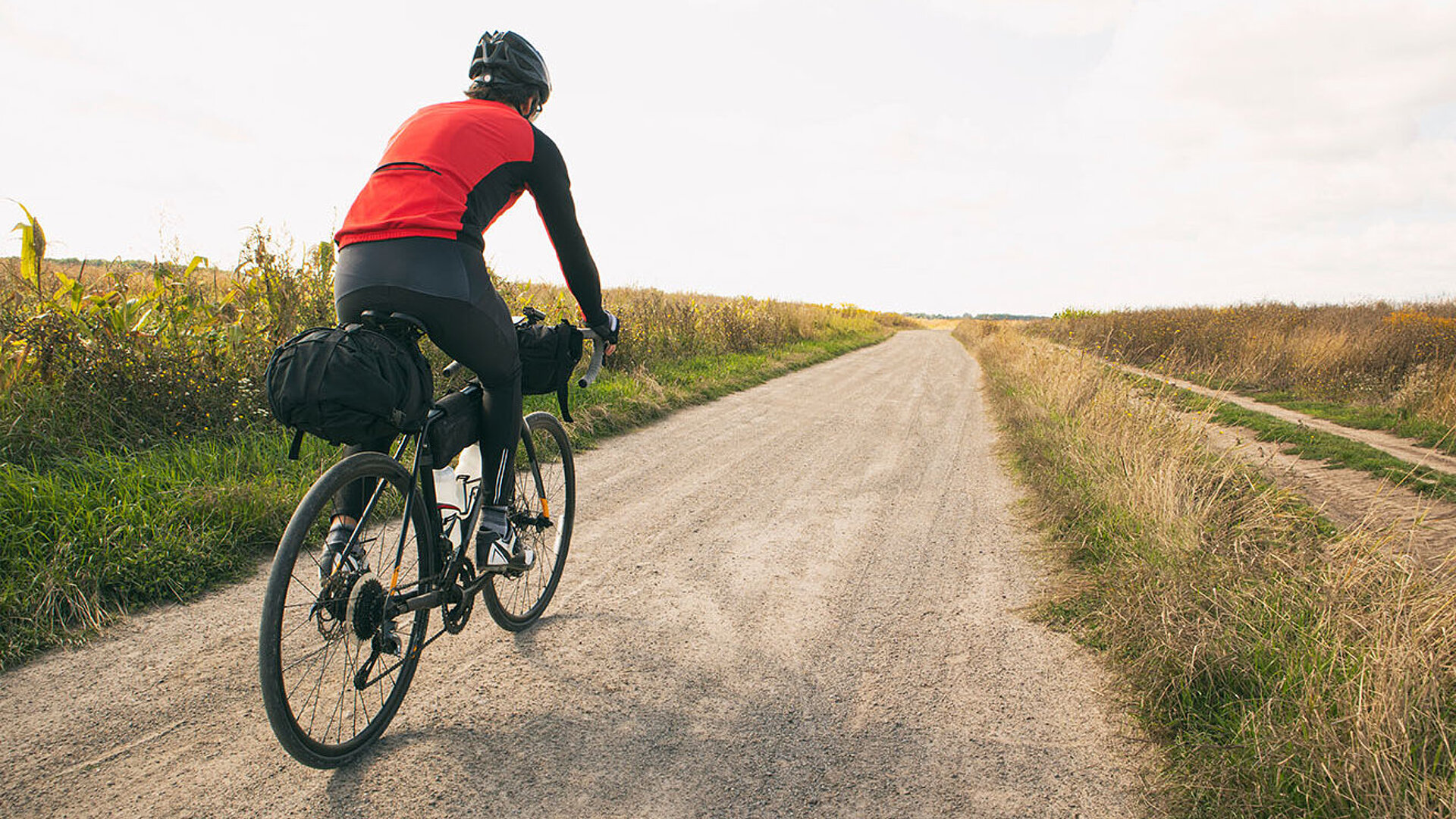 Person fährt mit dem Fahrrad auf einem Feldweg durch eine offene Landschaft.