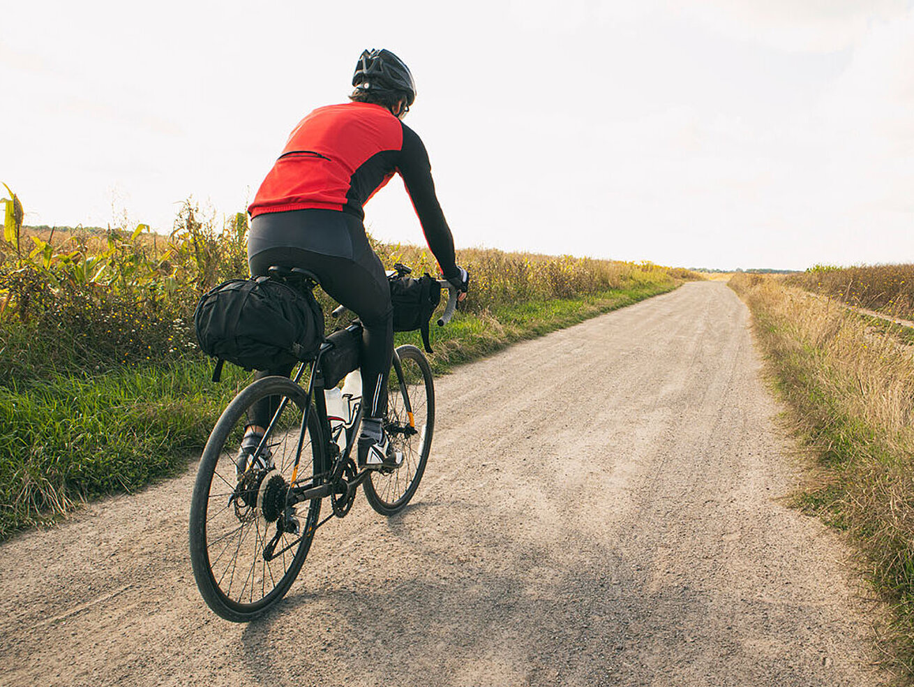 Person fährt mit dem Fahrrad auf einem Feldweg durch eine offene Landschaft.
