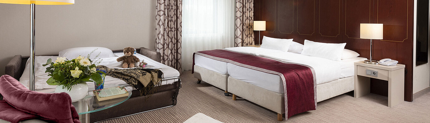 Comfort Familienzimmer Comfort Familienzimmer im Maritim Hotel Bonn mit großem Doppelbett, ausziehbarem Sofa, Sessel und Blumenarrangement.