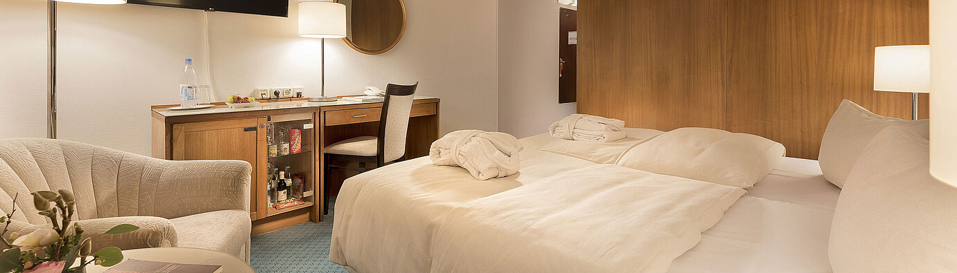 Classic Zimmer im Maritim Seehotel Timmendorfer Strand mit zwei Betten, Minibar, Schreibtisch, TV und Sitzgelegenheit.