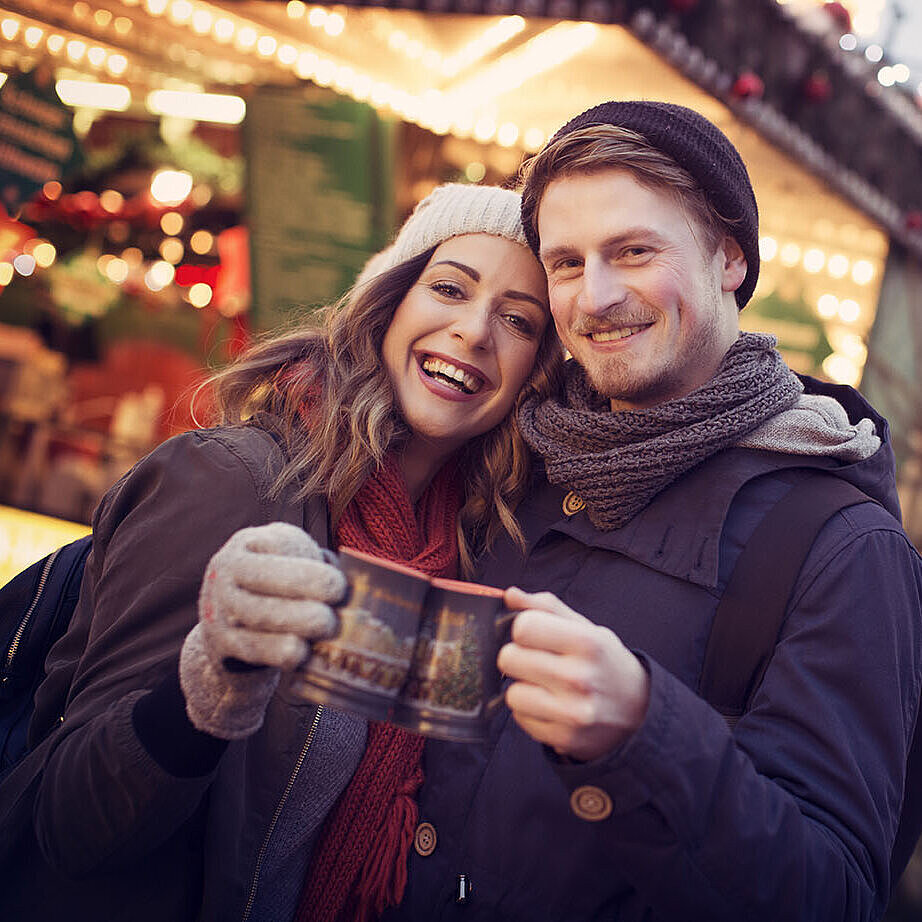 Paar stößt mit Glühwein auf einem festlich beleuchteten Weihnachtsmarkt an