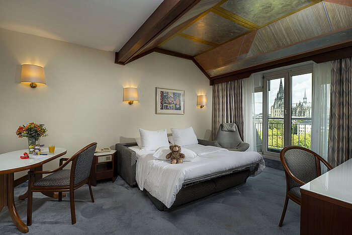 Gemütliches Familienzimmer im Maritim Hotel Köln mit Blick auf den Kölner Dom und Kuscheltieren auf dem Bett.