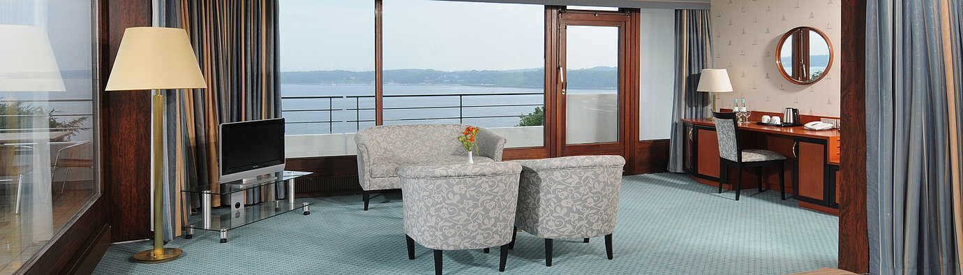 Junior Suite  Junior Suite im Maritim Hotel Kiel, mit Sitzecke, Schreibtisch, TV und großer Fensterfront mit Meerblick.