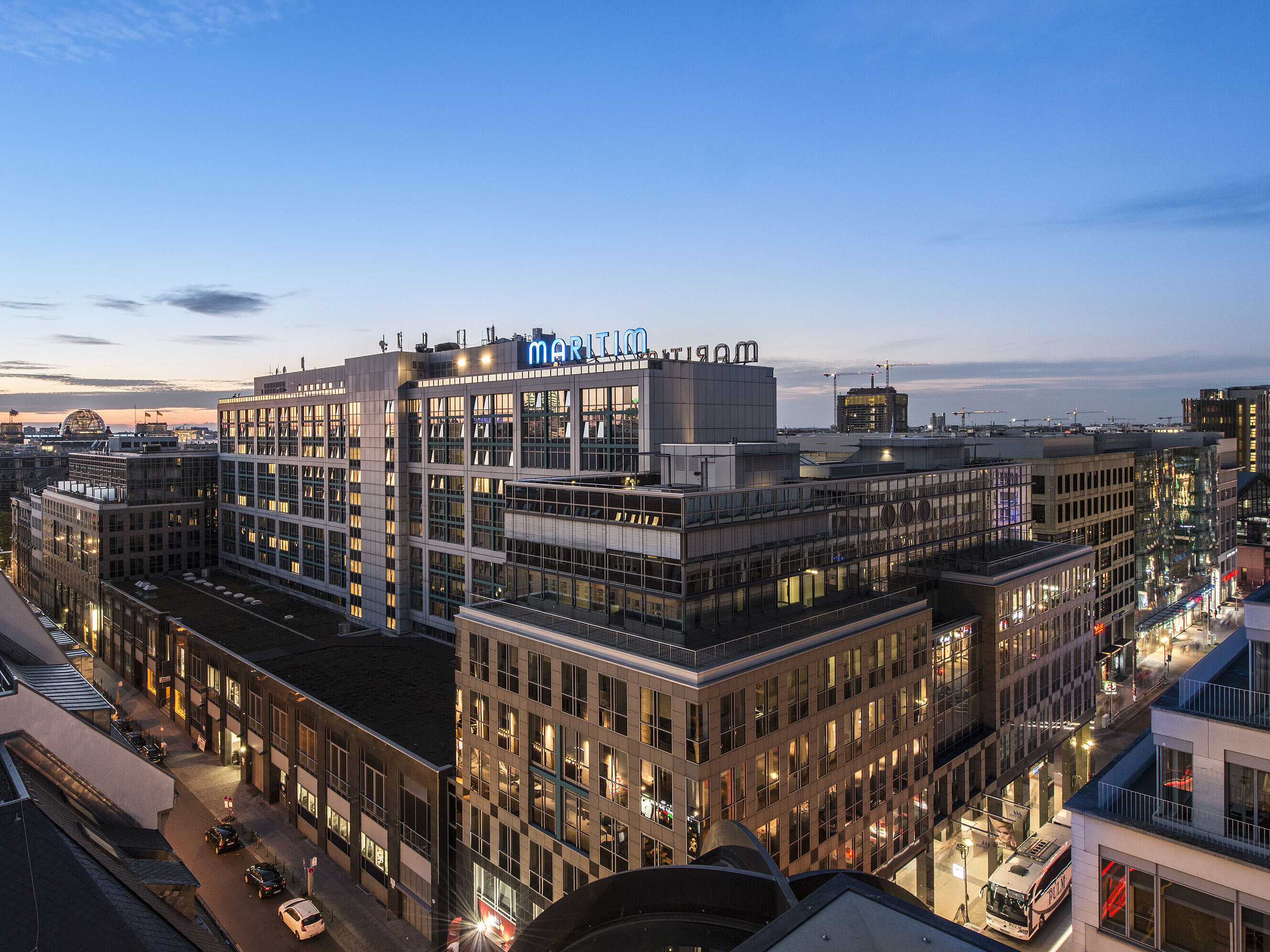 Blick auf das Maritim proArte Hotel Berlin bei Dämmerung, umgeben von modernen Gebäuden im Herzen Berlins.