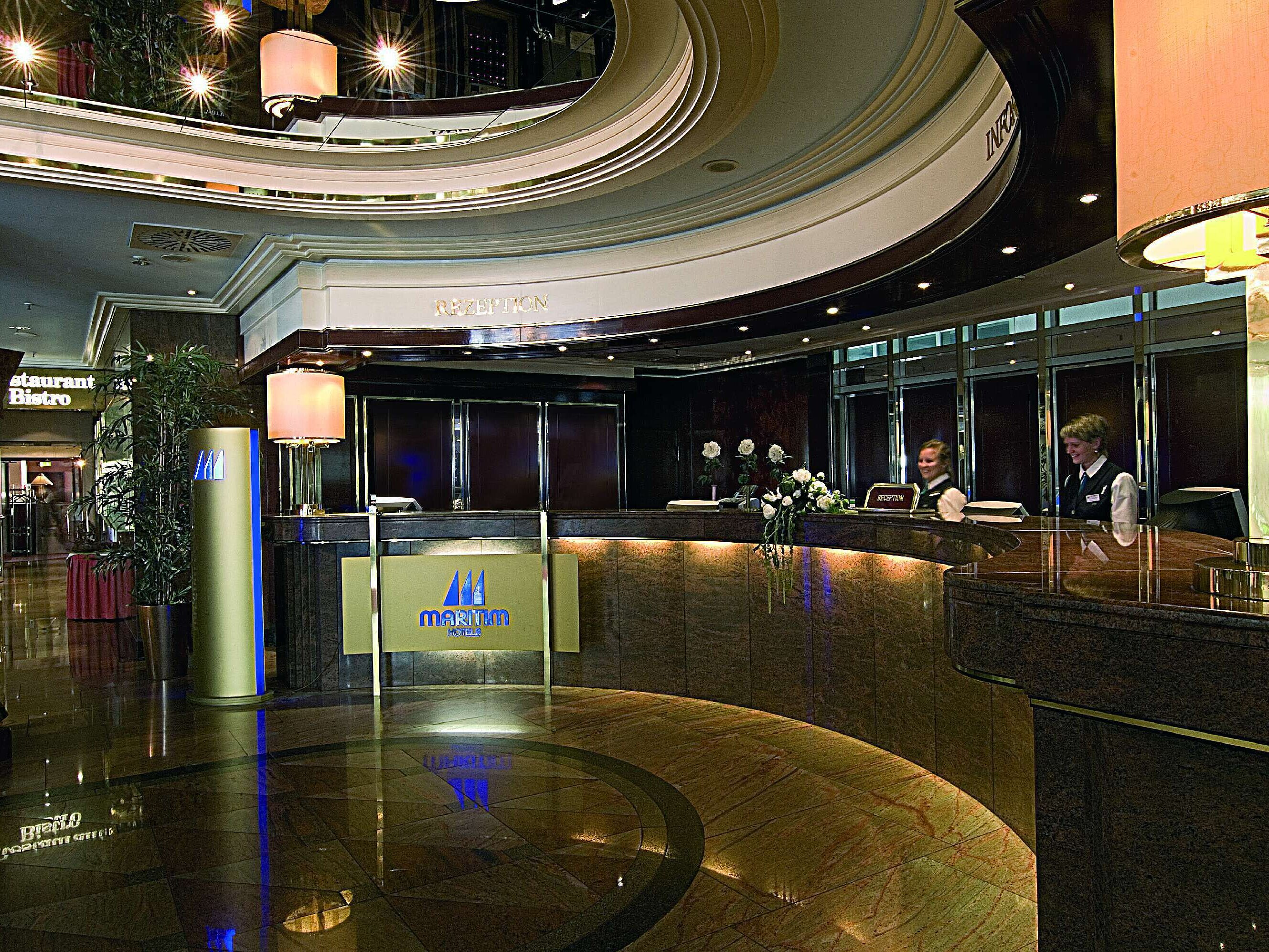 Elegante Lobby im Maritim Hotel München mit geschwungener Rezeption, Marmorboden und freundlichem Personal. 