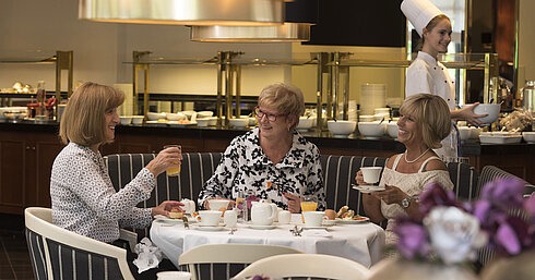 Drei Frauen genießen ein entspanntes Frühstück im Maritim Hotel Bad Homburg, bedient von einer freundlichen Köchin.