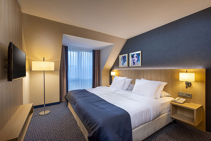 Modernes Doppelzimmer im Maritim Hotel Würzburg mit Kunst an der Wand und gemütlicher Beleuchtung.