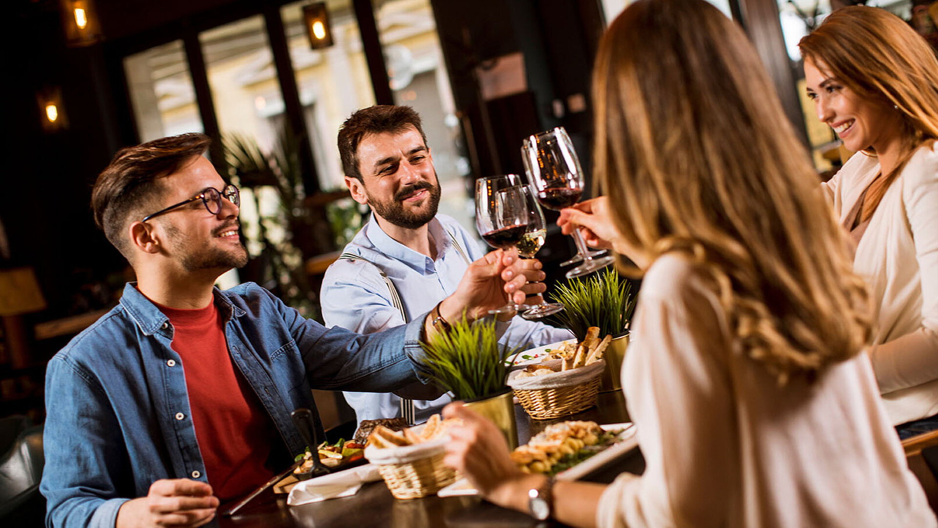 © BGSTock72 - AdobeStock.com Gruppe von Gästen genießt gemeinsam Speisen und Getränke in gemütlicher Atmosphäre an einem festlich gedeckten Tisch.