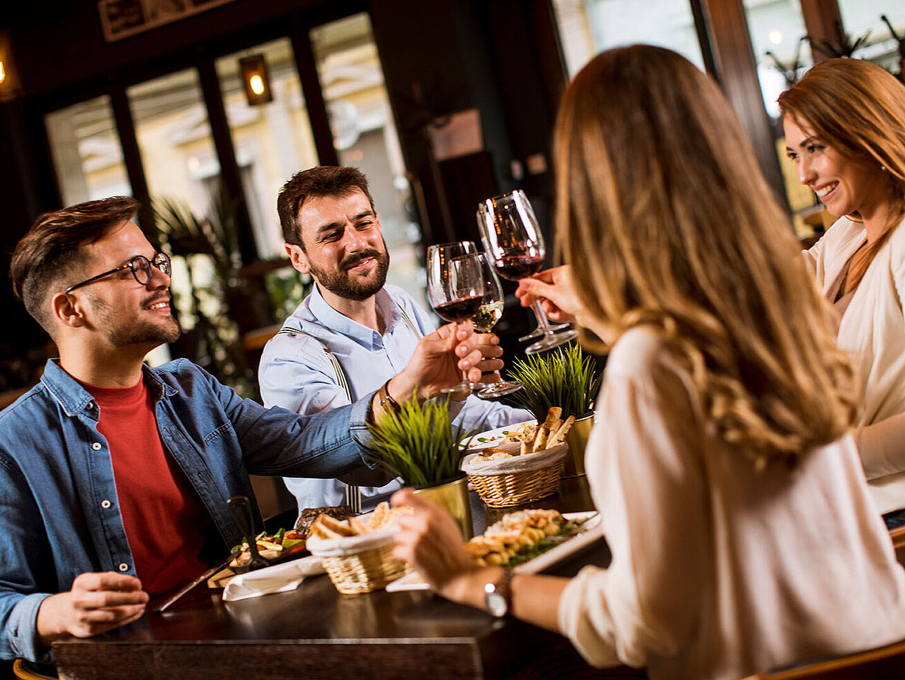 © BGSTock72 - AdobeStock.com Gruppe von Gästen genießt gemeinsam Speisen und Getränke in gemütlicher Atmosphäre an einem festlich gedeckten Tisch.