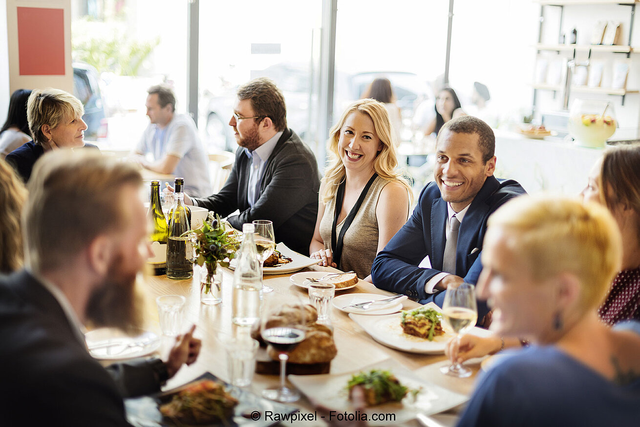 Kollegen sitzen gemeinsam am Tisch bei einer Firmenfeier und genießen Essen in geselliger Atmosphäre