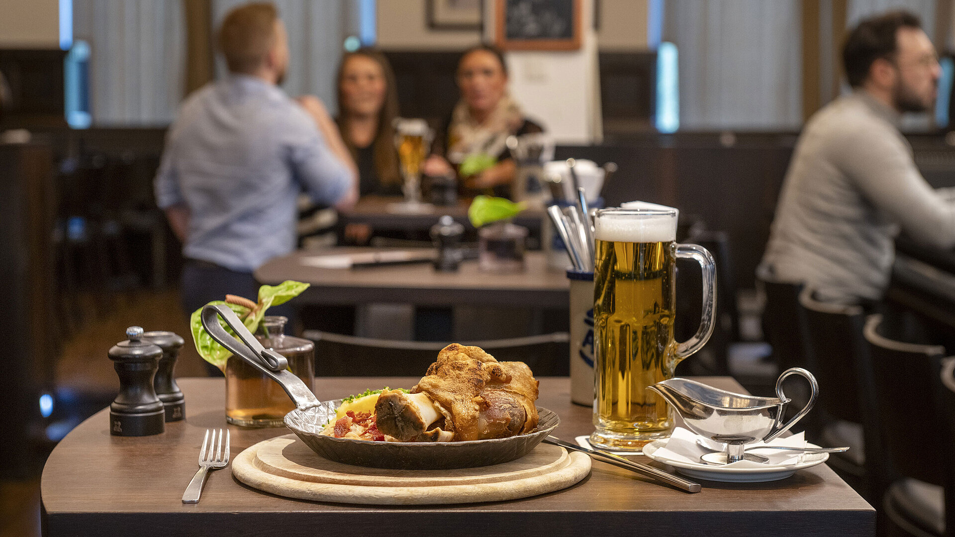 Rheinische Stov Servierter Schweinebraten mit Bier im Restaurant des Maritim Hotel Düsseldorf, im Hintergrund Gäste in geselliger Atmosphäre.