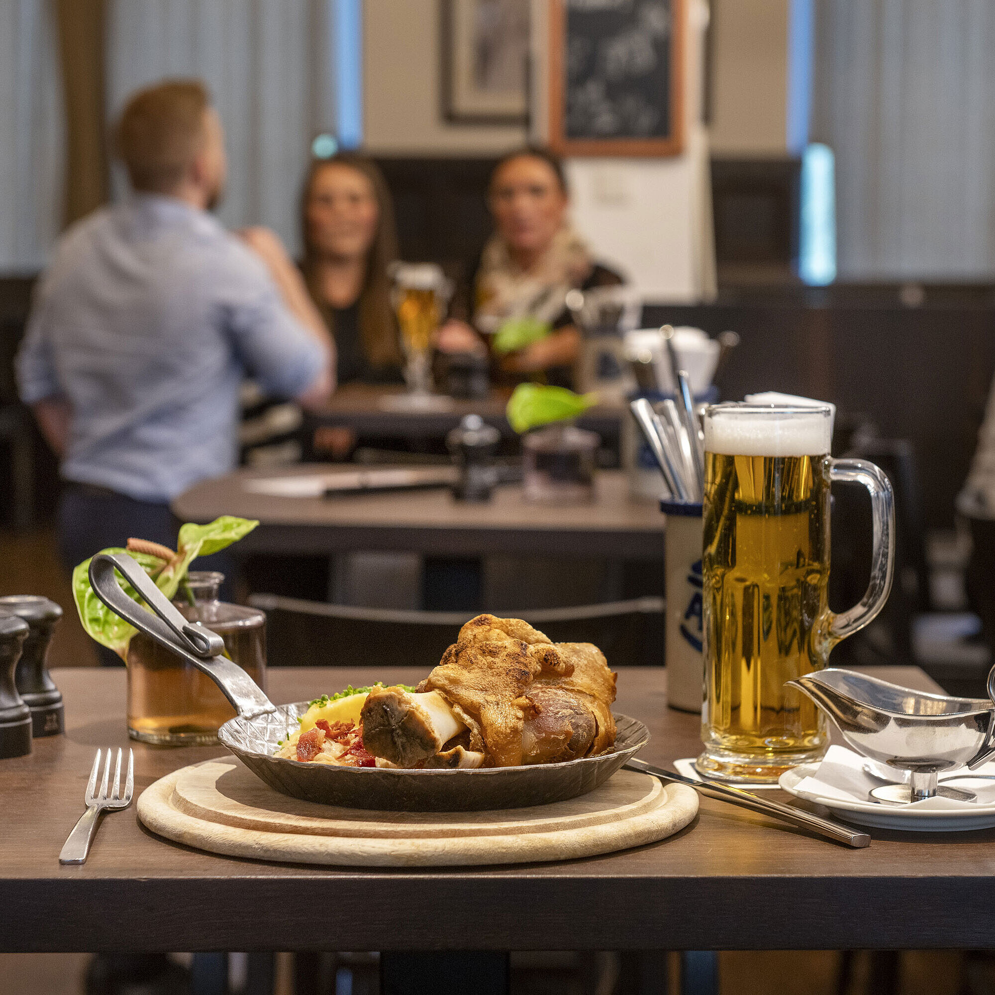 Rheinische Stov Servierter Schweinebraten mit Bier im Restaurant des Maritim Hotel Düsseldorf, im Hintergrund Gäste in geselliger Atmosphäre.