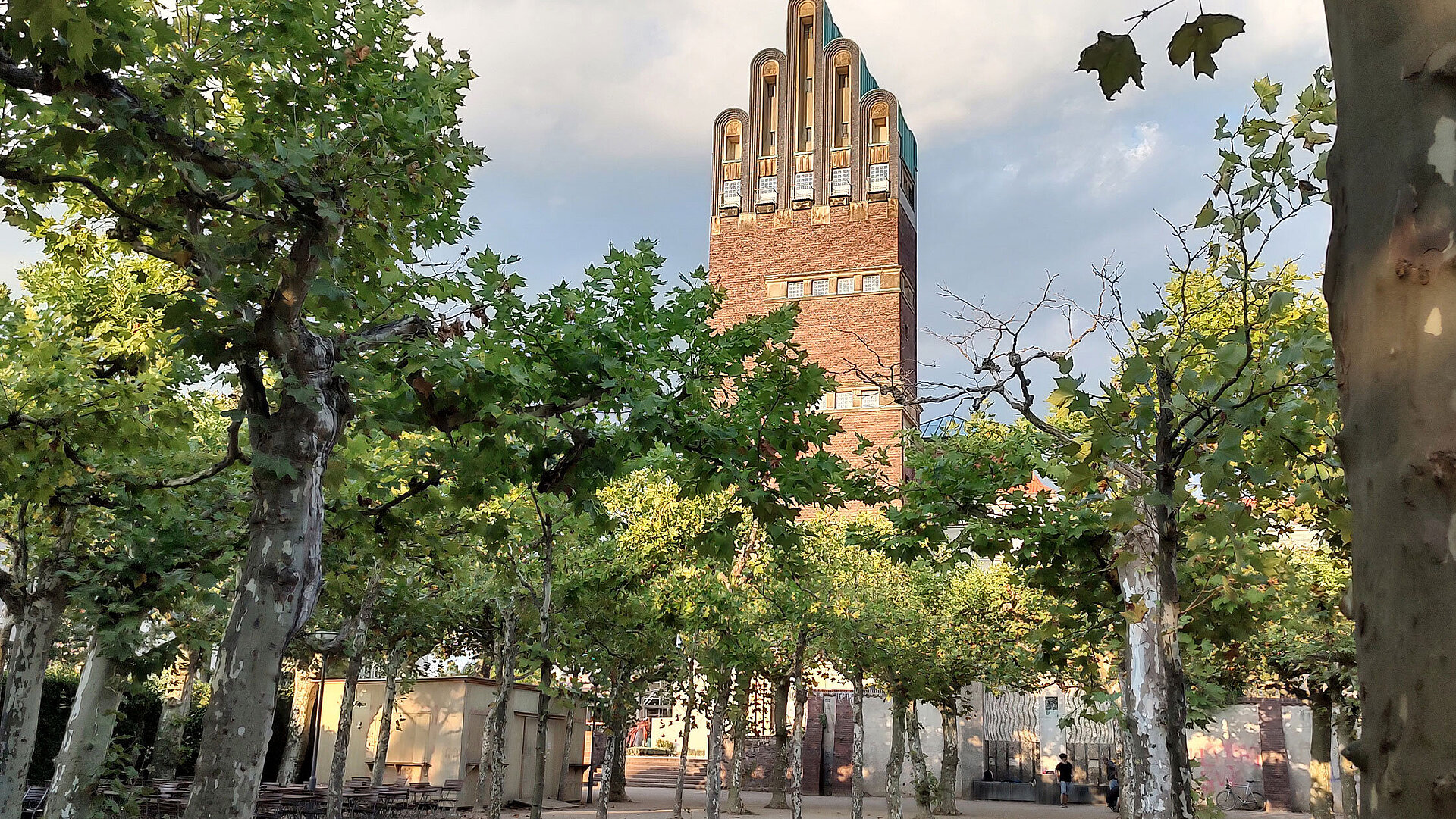 UNESCO Welterbe Mathildenhöhe Blick auf den Hochzeitsturm auf der Mathildenhöhe in Darmstadt, umgeben von Platanen und blauem Himmel.