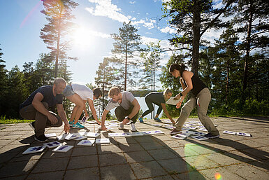 Gruppe von Erwachsenen beim Outdoor-Teambuilding macht gemeinsame Fitnessübung im Wald bei Sonnenschein