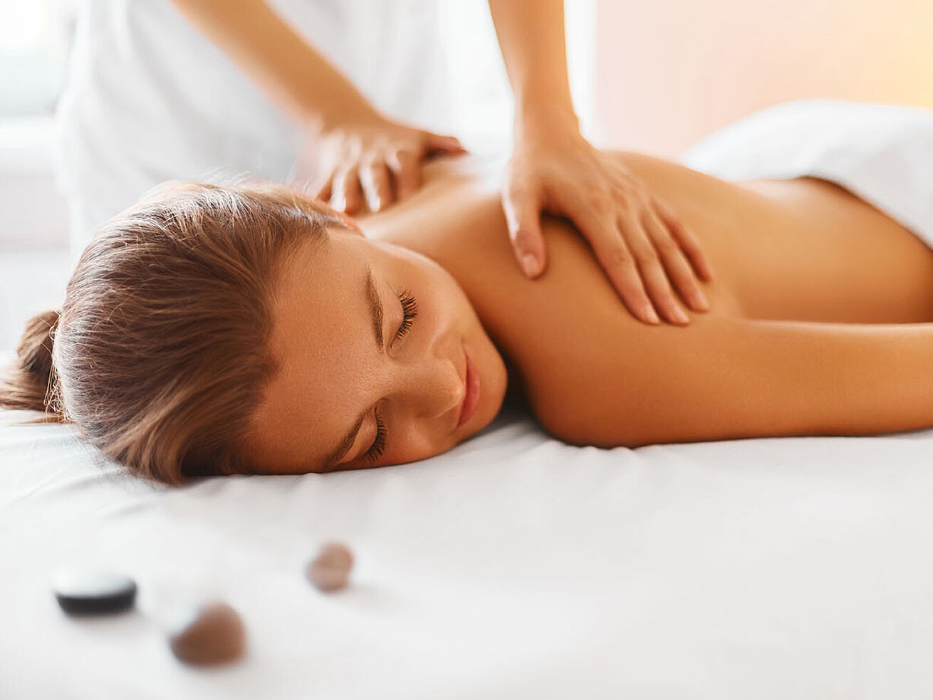Frau genießt entspannende Rückenmassage im Spa mit warmem Licht und Steinen