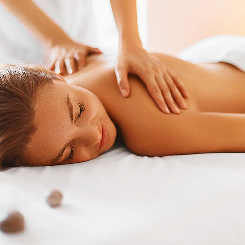 Frau genießt entspannende Rückenmassage im Spa mit warmem Licht und Steinen