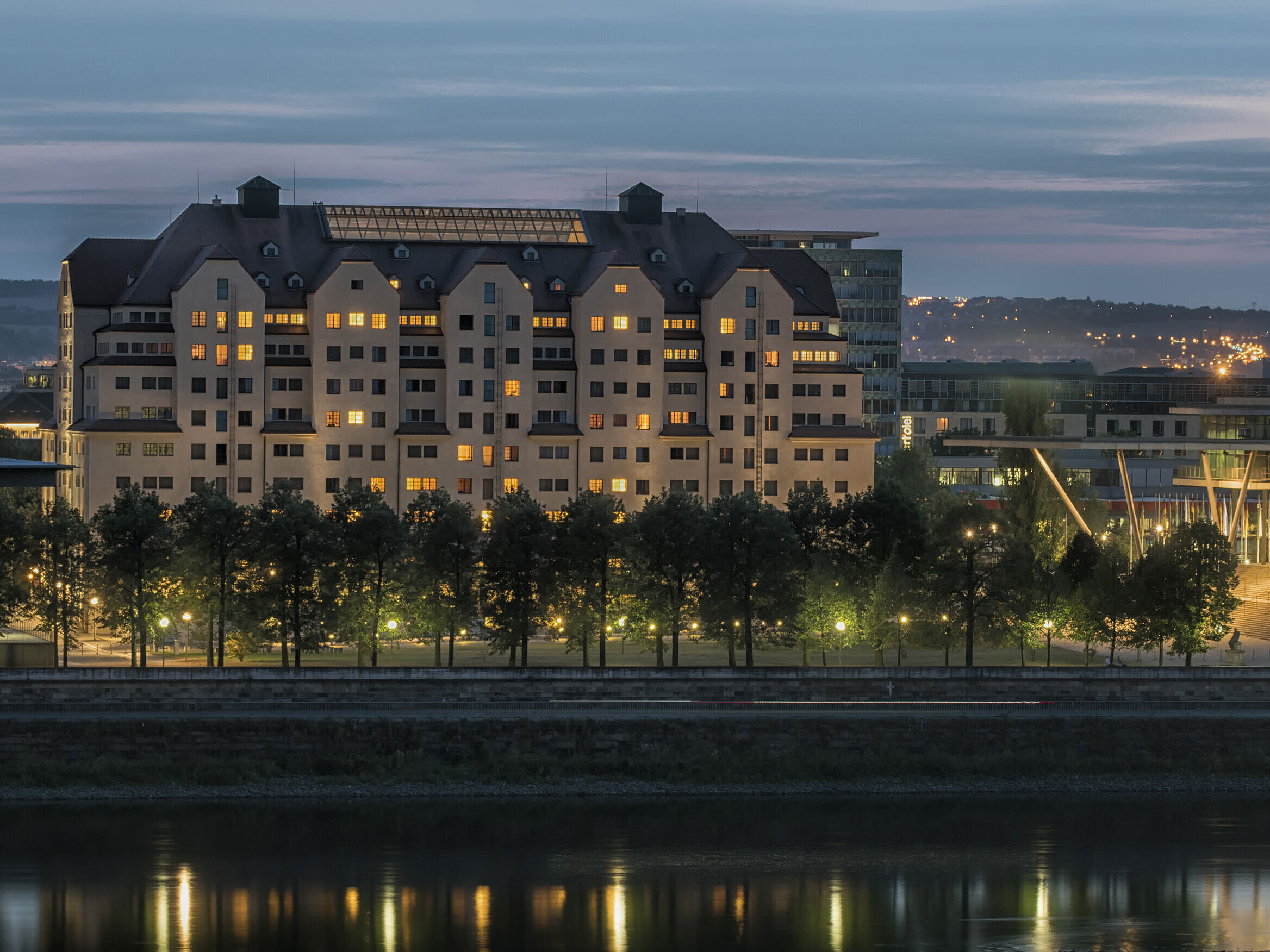 Beleuchtetes Maritim Hotel Dresden bei Dämmerung mit reflektierenden Lichtern auf der Elbe.