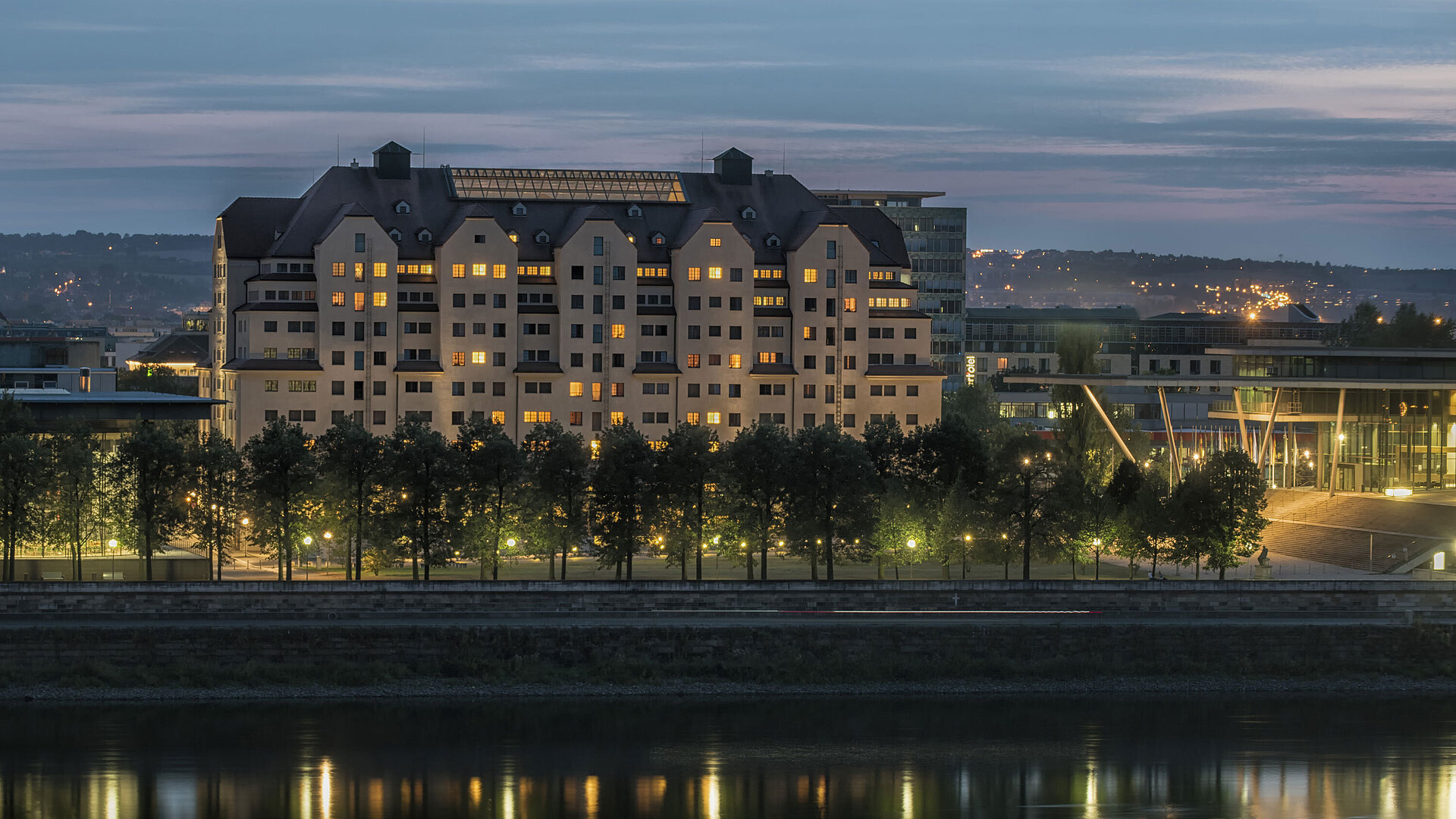 Außenansicht bei Nacht Beleuchtetes Maritim Hotel Dresden bei Dämmerung mit reflektierenden Lichtern auf der Elbe.