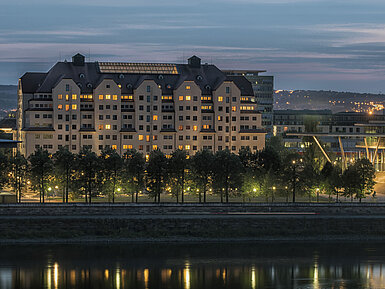 Beleuchtetes Maritim Hotel Dresden bei Dämmerung mit reflektierenden Lichtern auf der Elbe.