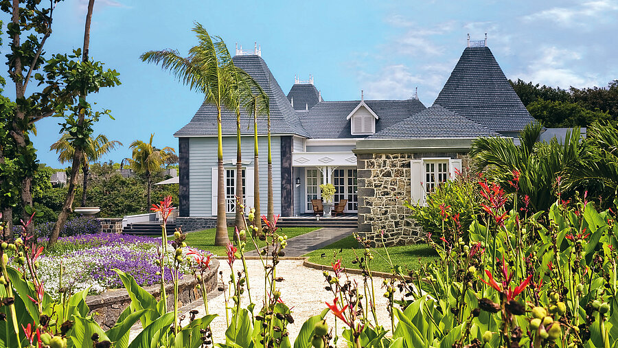 Außenansicht Elegante tropische Villa mit Palmen, gepflegtem Garten und heller Fassade bei Sonnenschein