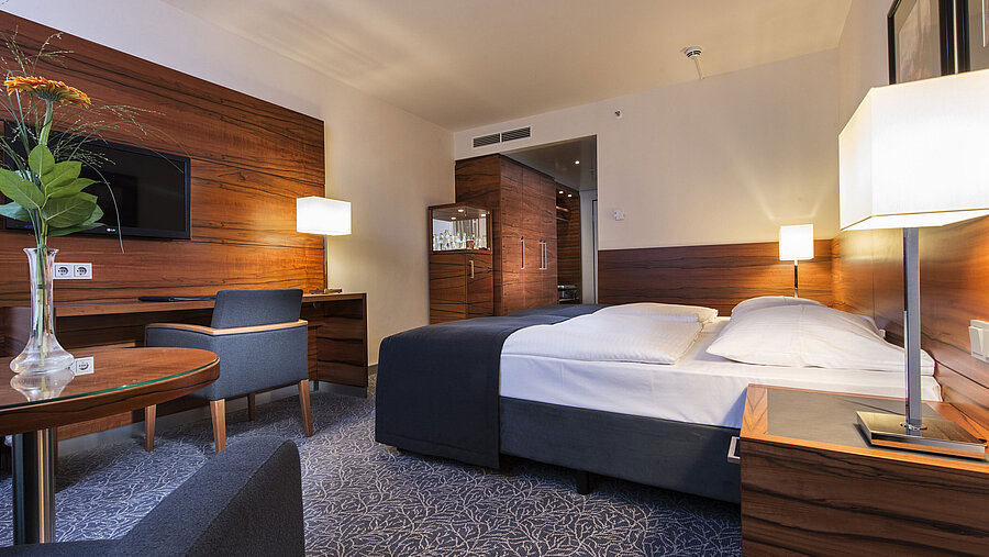 Eingerichtetes Hotelzimmer im Maritim Hotel München mit komfortablem Bett, Arbeitsbereich, TV und Holzverkleidung.