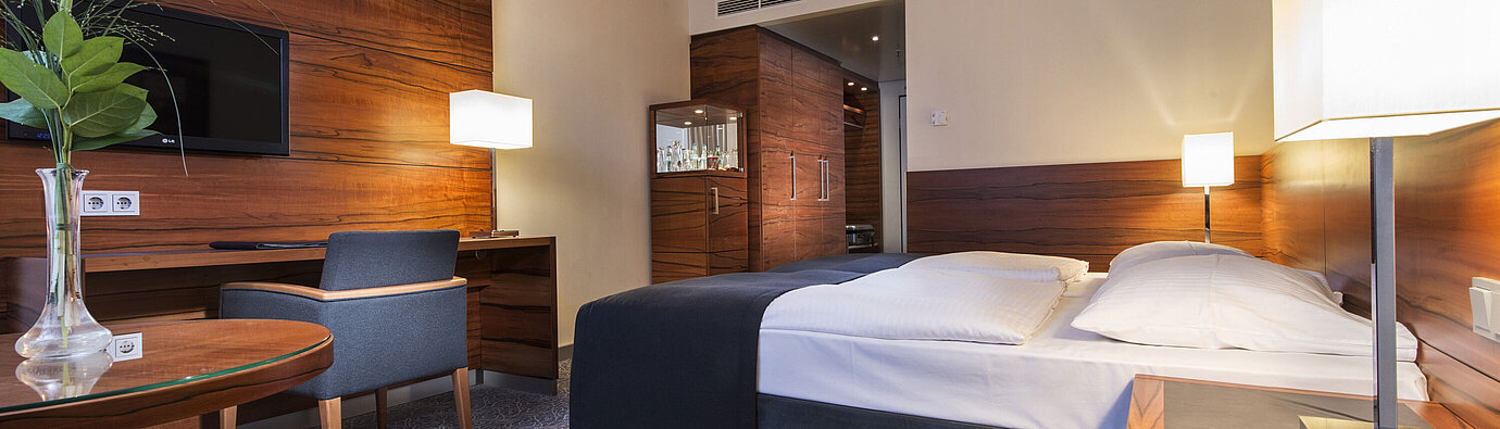 Eingerichtetes Hotelzimmer im Maritim Hotel München mit komfortablem Bett, Arbeitsbereich, TV und Holzverkleidung.