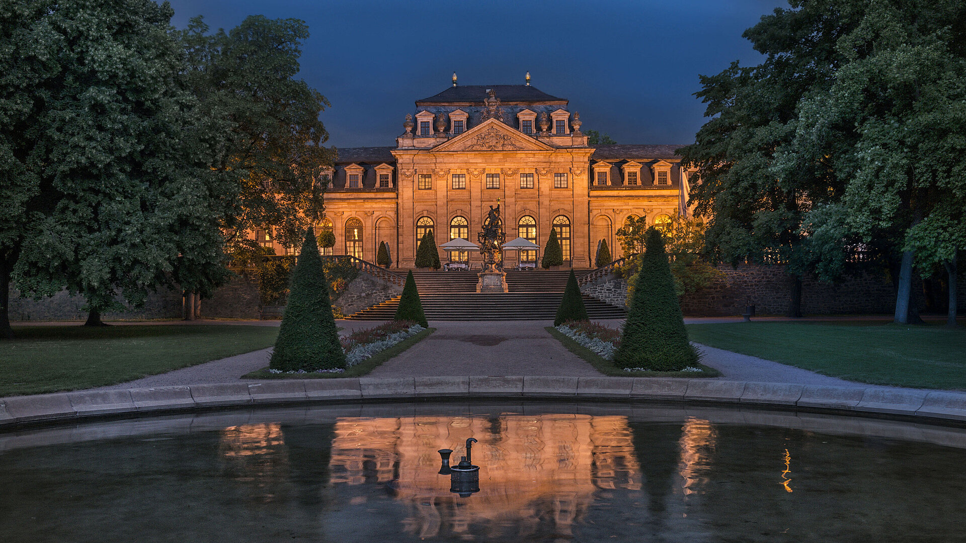 Das Maritim Hotel Fulda, eindrucksvoll beleuchtet bei Nacht, mit Spiegelung im Wasserbecken des Barockgartens.