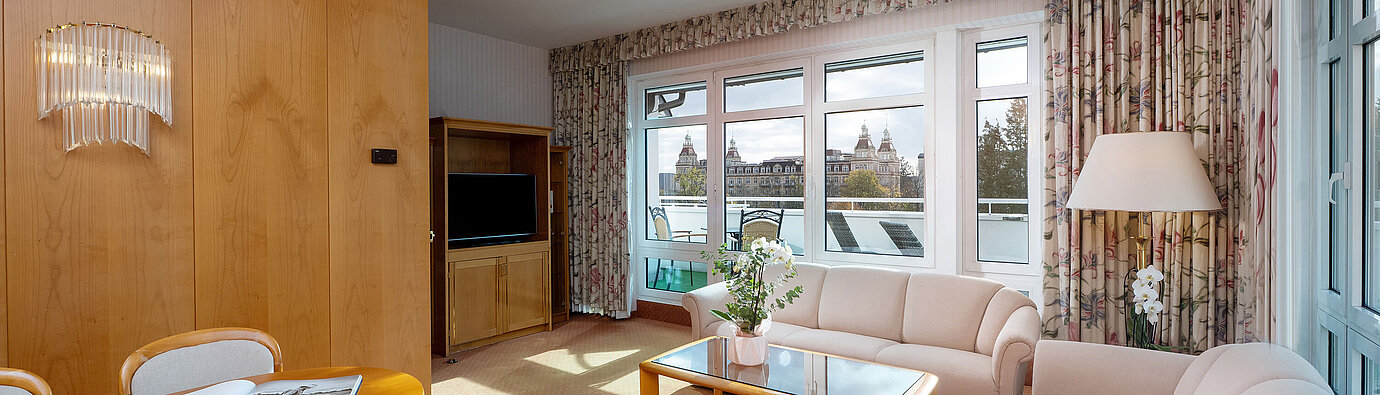 Junior Suite mit hellem Wohnbereich, Sofa, großem Fenster, Essplatz und klassischer Einrichtung im Maritim Hotel.
