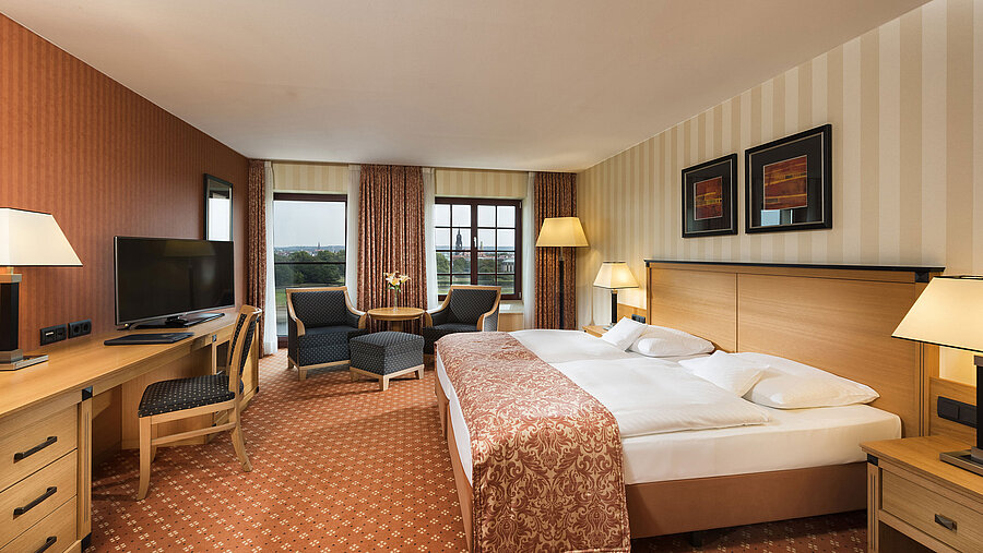 Superior Zimmer im Maritim Hotel Dresden mit elegantem Doppelbett, Schreibtisch und Sitzbereich sowie Blick auf die Stadt.