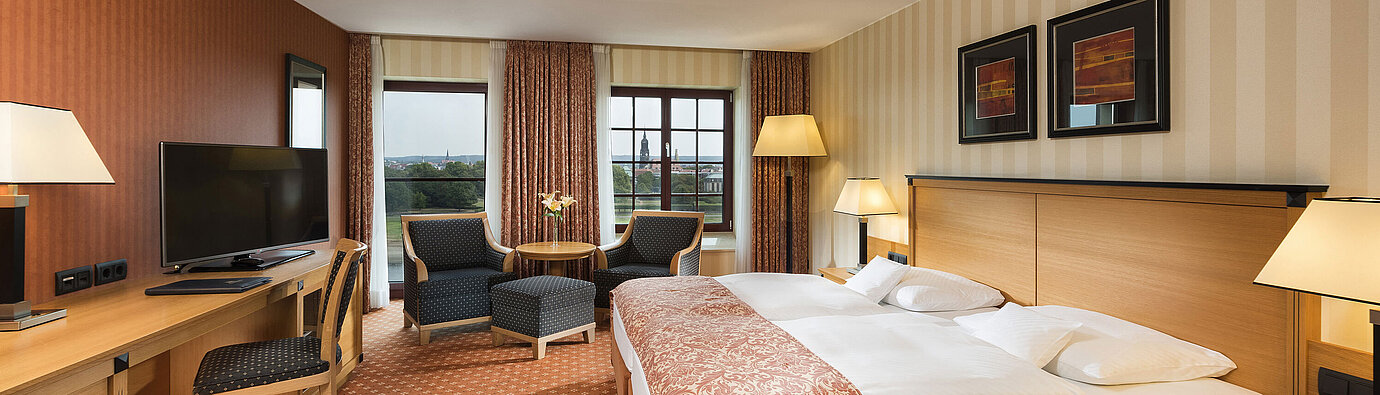 Superior Zimmer Superior Zimmer im Maritim Hotel Dresden mit elegantem Doppelbett, Schreibtisch und Sitzbereich sowie Blick auf die Stadt.