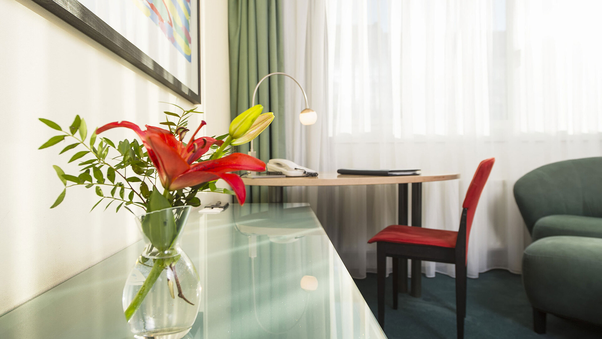 Elegantes Classic-Zimmer im Maritim Berlin, dekoriert mit einer roten Blume in einer Vase, Schreibtisch und Sitzgelegenheit.