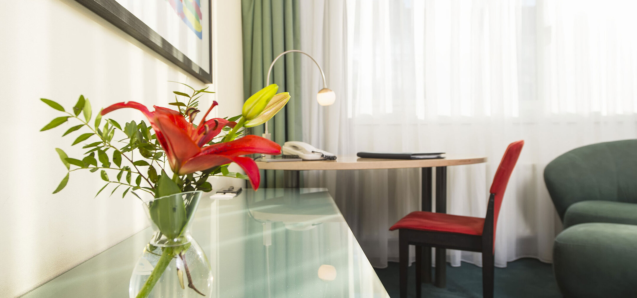 Elegantes Classic-Zimmer im Maritim Berlin, dekoriert mit einer roten Blume in einer Vase, Schreibtisch und Sitzgelegenheit.