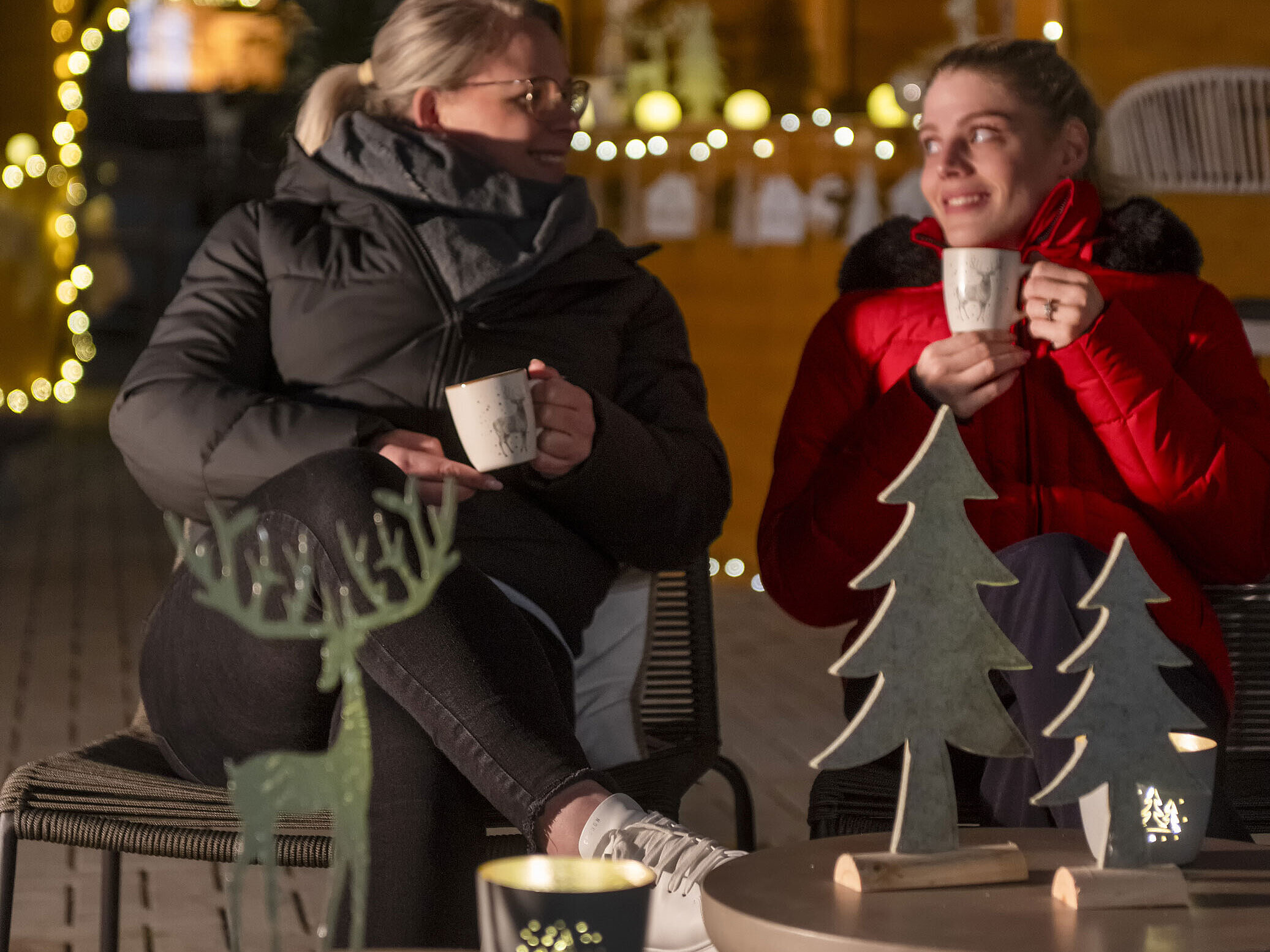 Zwei Frauen genießen heiße Getränke auf dem Weihnachtsmarkt des Maritim Hotels mit stimmungsvoller Dekoration im Hintergrund.