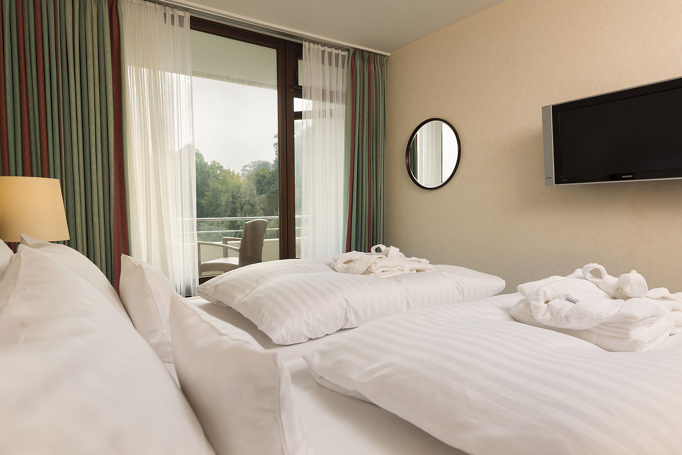 Doppelbett mit TV, Bademantel und Ausblick auf den Balkon im Maritim Hotel Bad Salzuflen