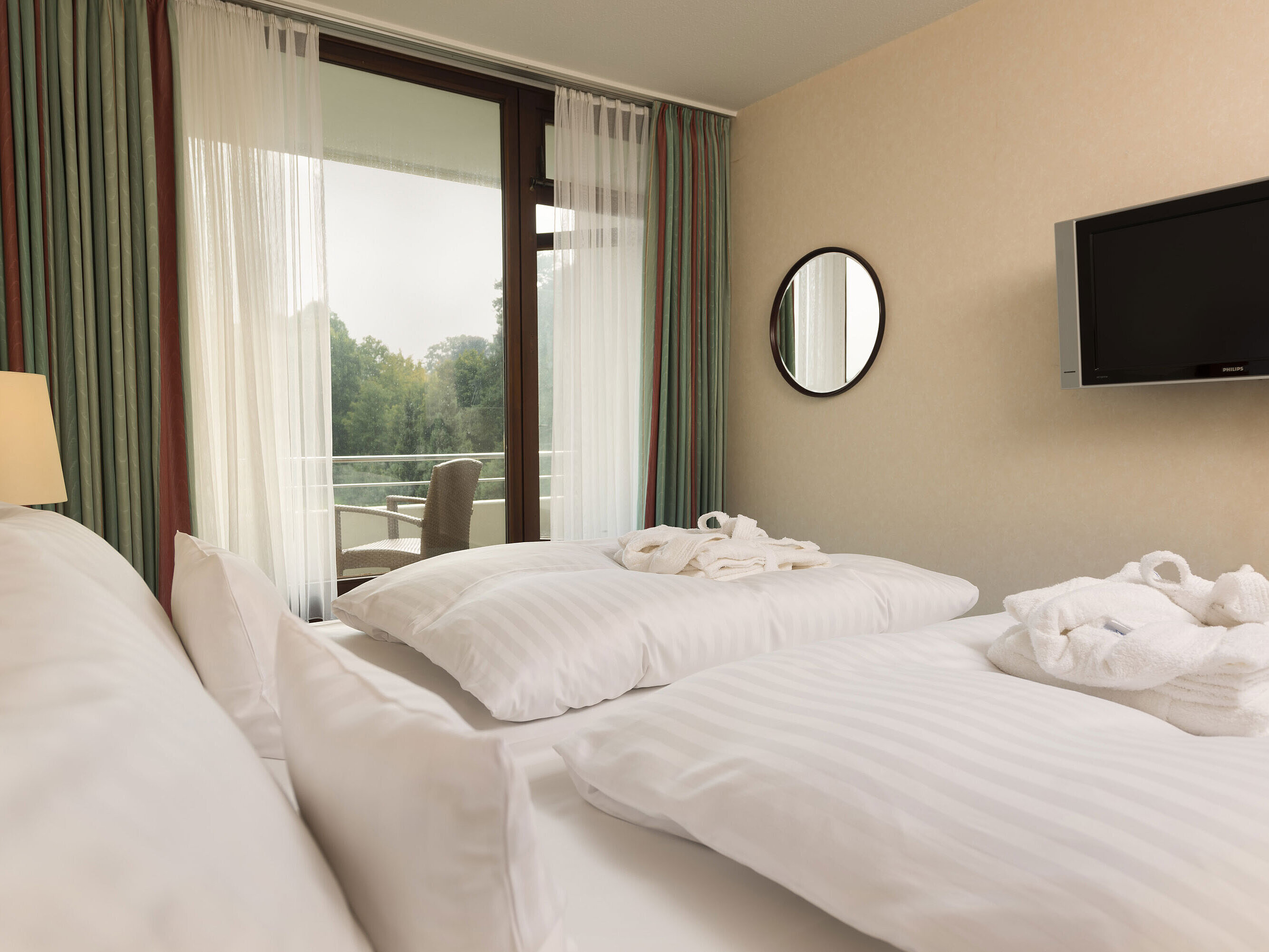 Doppelbett mit TV, Bademantel und Ausblick auf den Balkon im Maritim Hotel Bad Salzuflen