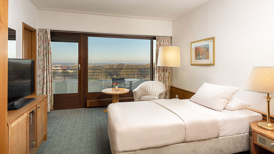 Einzelzimmer mit bequemen Bett, Sessel und Balkon mit Ausblick auf Travemünde und die Lübecker Bucht