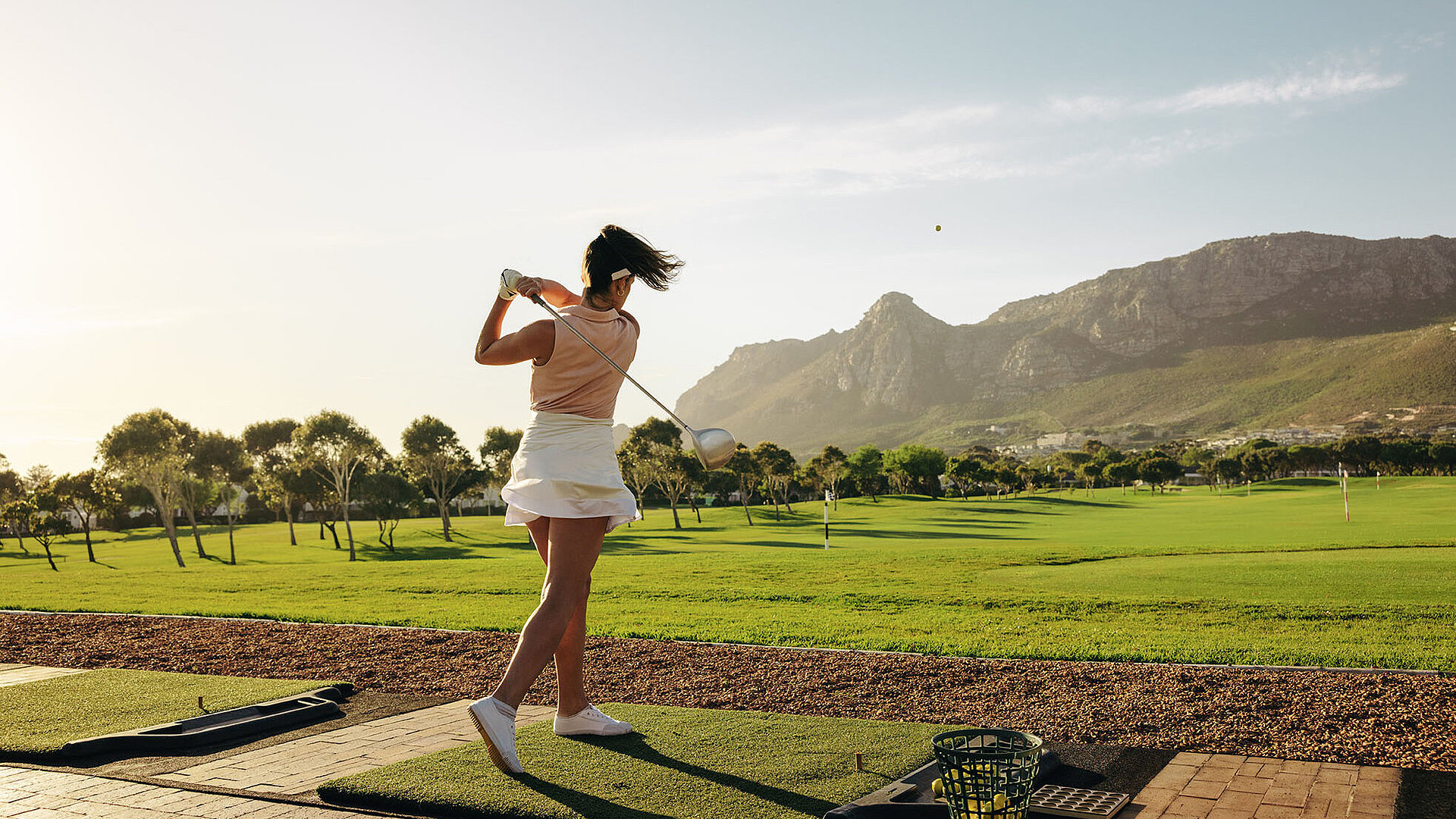 © Jacob Lund - AdobeStock.com Golferin nach dem Abschlag auf einem Golfplatz mit Blick auf Fairway und Berglandschaft.
