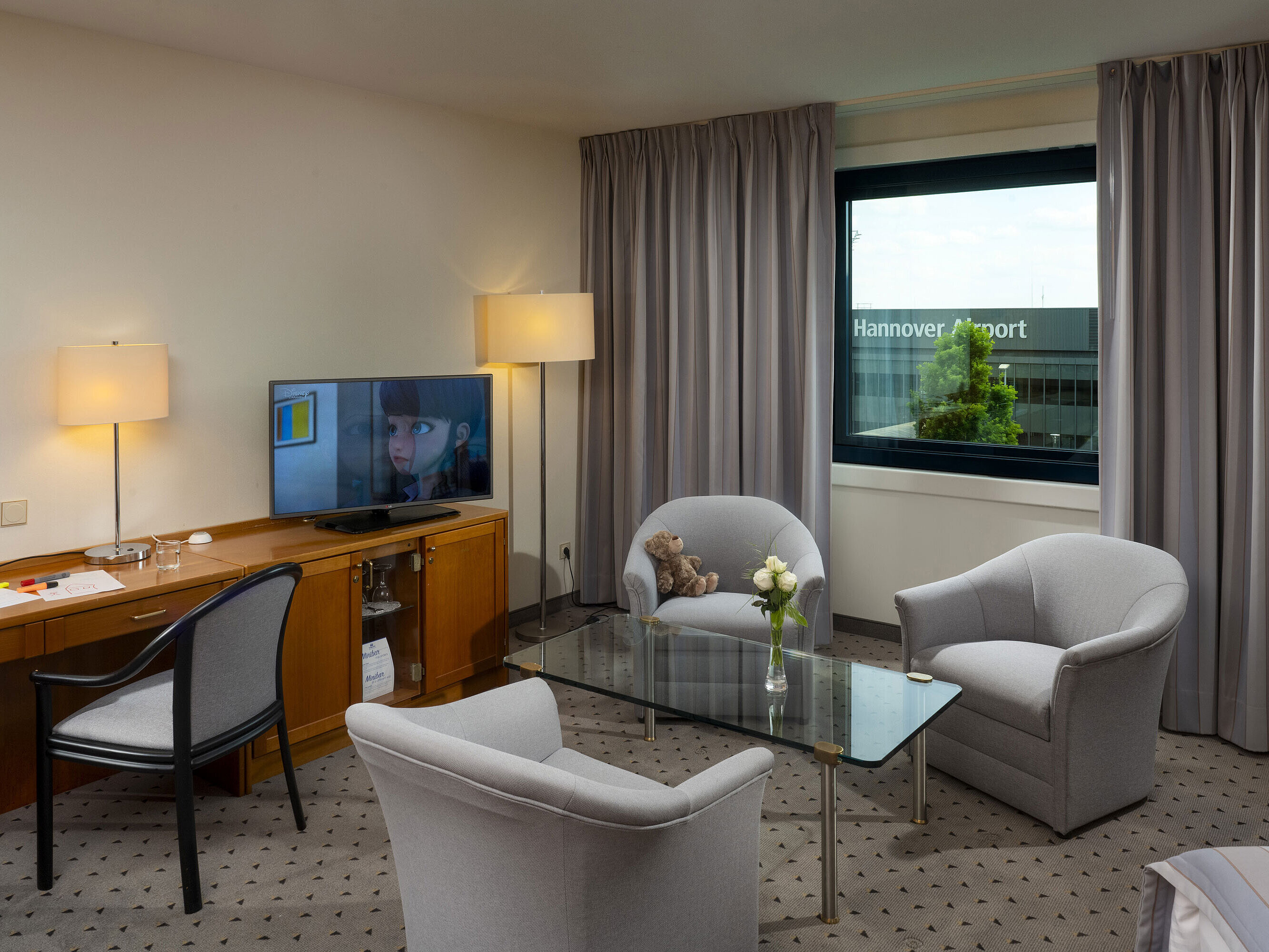 Komfortables Familienzimmer mit Sitzbereich, TV und Ausblick auf den Hannover Airport im Maritim Hotel Hannover.