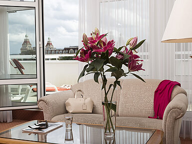 Helles Wohnzimmer mit Blumen, Sofa und Blick auf die historischen Türme vom Balkon im Maritim Hotel Bad Wildungen