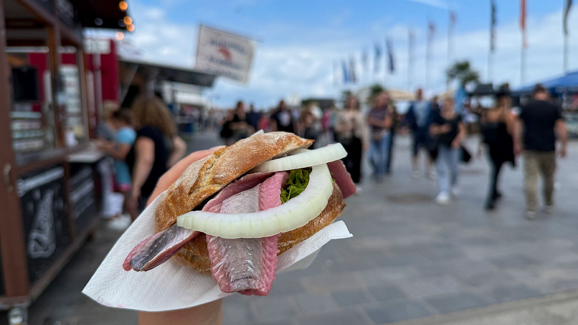 © Lapasmile - AdobeStock.com Frisches Fischbrötchen mit Zwiebeln und Fischfilet an einem Imbissstand an der Promenade.