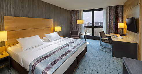 Comfort Zimmer im Maritim Hotel Düsseldorf mit großem Doppelbett, Schreibtisch, Sessel und Panoramafenster.