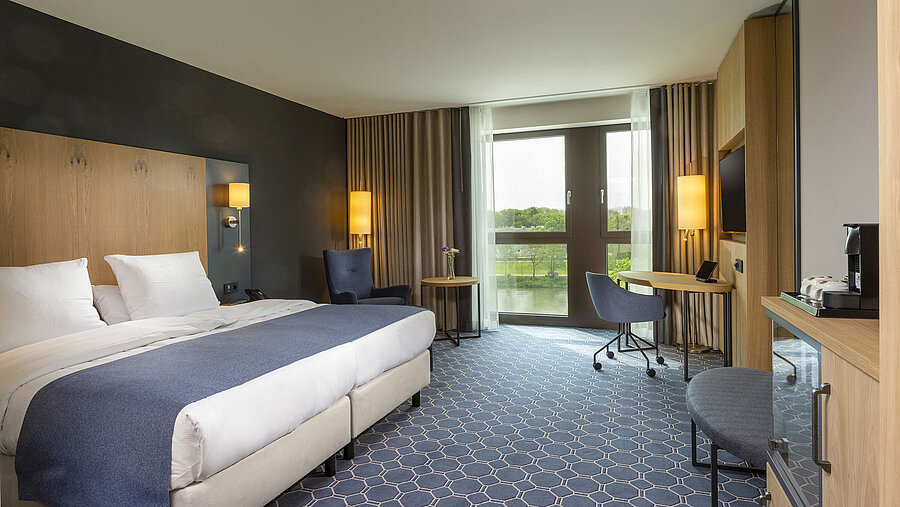 Geräumiges Doppelzimmer im Maritim Hotel Ingolstadt mit großem Bett, Schreibtisch und Blick auf den Fluss.