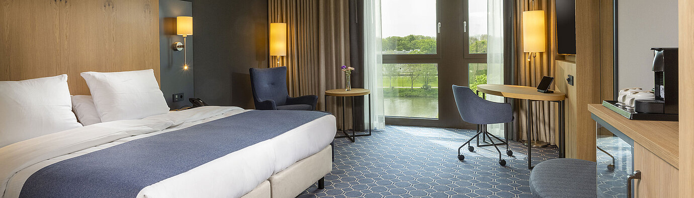 Geräumiges Doppelzimmer im Maritim Hotel Ingolstadt mit Bett, Schreibtisch und Blick auf den Fluss.