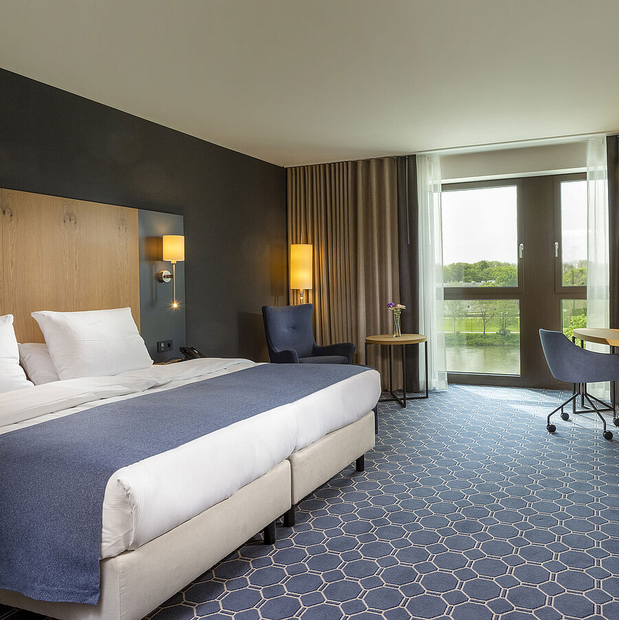 Geräumiges Doppelzimmer im Maritim Hotel Ingolstadt mit großem Bett, Schreibtisch und Blick auf den Fluss.