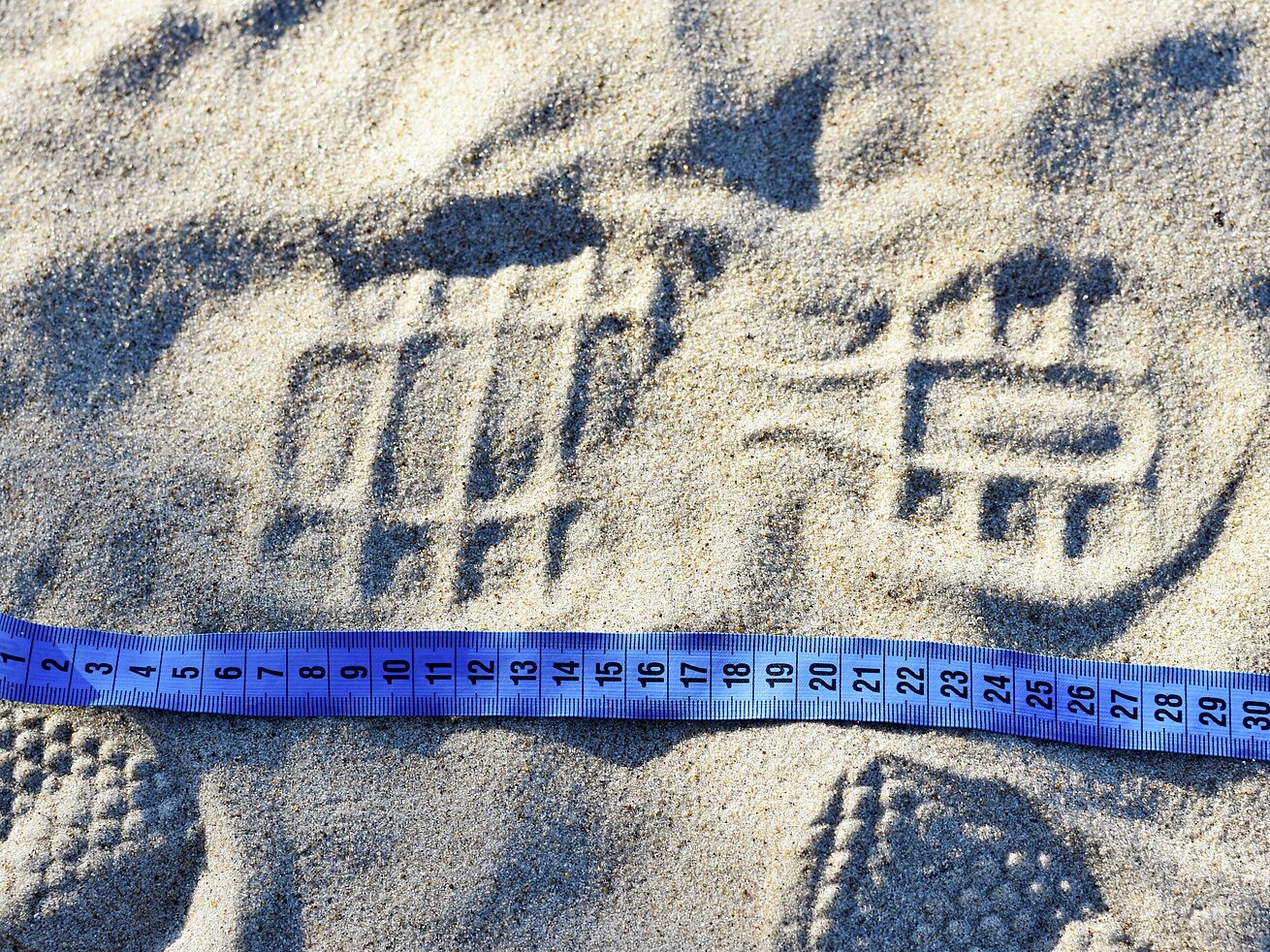 Fußabdruck im Sand Ein tiefer Schuhabdruck im Sand neben einem blauen Maßband.