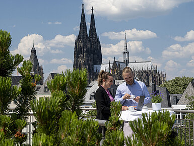 Zwei Personen arbeiten und genießen Kaffee auf der Dachterrasse des Maritim Hotels Köln mit Blick auf den Kölner Dom.